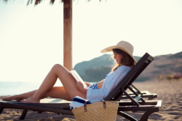 A woman on a beach sun lounger reading a book in her bikini with an oversized hat, with a beach bag resting by her side. Ross Woodhall - Action & Lifestyle Photography