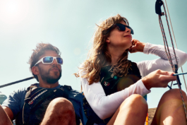 A close up of a couple on a sailing boat taking in the view, wearing life vests. Ross Woodhall - Action & Lifestyle Photography