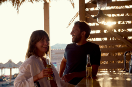 Couple enjoying a drink at sunset by the beach bar. with beach grass umbrellas in the background. Ross Woodhall - Action & Lifestyle Photography