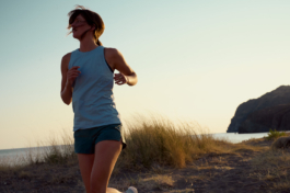 Woman jogging along the coastline in a tank top and pair of shorts with gentle breeze in her hair and the late evening sun behind her. Ross Woodhall - Action & Lifestyle Photography