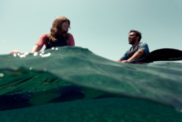 A couple gazing towards each other, taking a break from kayaking in the sea, seen halfway through a wave in the water. Ross Woodhall - Action & Lifestyle Photography