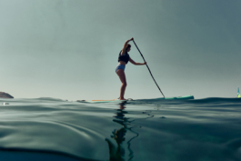 Woman paddle boarding on calm water on the sea. with a life jacket on and paddle. Ross Woodhall - Action & Lifestyle Photography