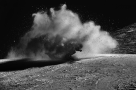 Black and white image of a snowboarder coming towards the camera with snow in the air around him. Ross Woodhall - Action & Lifestyle Photography