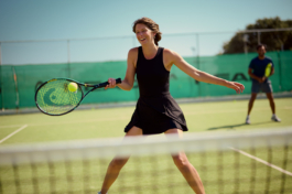 Couple playing doubles, tennis outside with woman in the foreground, smiling just about to hit the tennis ball. Ross Woodhall - Action & Lifestyle Photography