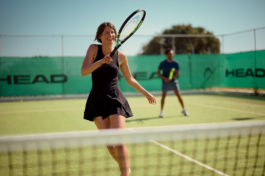 Couple playing doubles, tennis outside with the woman in the foreground smiling after just hitting the ball. Ross Woodhall - Action & Lifestyle Photography
