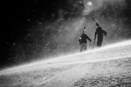 Black and white of two skiers walking away from the camera up hill on a blustery day, with snow particles in the air. Ross Woodhall - Action & Lifestyle Photography