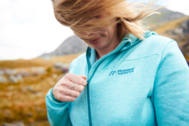 close up of woman mid zip on her hoody, whilst hiking with her hair caught across her face, due to the wind. Ross Woodhall - Action & Lifestyle Photography