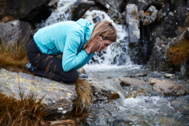 Woman crouched, holding her hair back over a stream. Ross Woodhall - Action & Lifestyle Photography