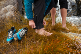 two hikers going bare foot, taking off their hiking shoes by the stream in the rough grass. Ross Woodhall - Action & Lifestyle Photography