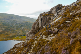 two hikers walking down a steep hill on a stone path with autumnal colours with a lake down in the valley. Ross Woodhall - Action & Lifestyle Photography