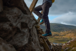 Hiker going over a wooden stile on a stone wall up in the hills, with a lake down in the distance. Ross Woodhall - Action & Lifestyle Photography