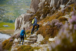 A couple hiking, walking uphill on stone steps with rocks and heather. lake and hill in the background. Ross Woodhall - Action & Lifestyle Photography