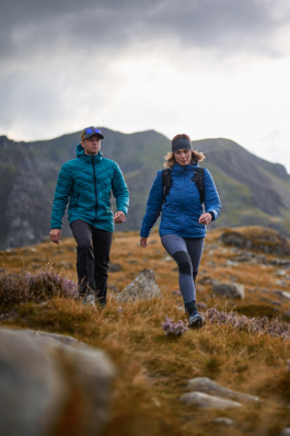 Couple hiking across the rough grass with heather, with hills in the background. Ross Woodhall - Action & Lifestyle Photography