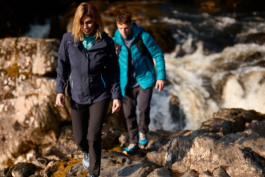 Couple out hiking along a river, stream with full hiking kit on, on a rocky path. Ross Woodhall - Action & Lifestyle Photography
