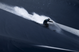 off piste skier, at start of turn with left pole out stretched, caught in a shaft of sunlight with the snow caught by the wind Ross Woodhall - Action & Lifestyle Photography