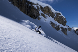 Off piste skier going downhill with cliff,rock edge in background Ross Woodhall - Action & Lifestyle Photography
