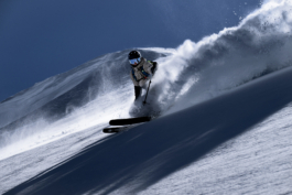 skier off piste with left pole out turning towards the camera, front of skis poked out of snow with snow kicked up, caught by the wind, cornice in the background. Ross Woodhall - Action & Lifestyle Photography