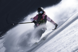 close up of female skier wearing pink jacket turning with pole out, flicked up snow caught in the wind. Ross Woodhall - Action & Lifestyle Photography