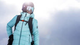 female skier looking out with googles and helmet on with sun directly behind her. Wearing a bright light blue puffy style jacket. Ross Woodhall - Action & Lifestyle Photography