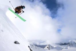 skier off piste mid air off steep mountain side with a right hand grab. Mountains and clouds in the background. Ross Woodhall - Action & Lifestyle Photography